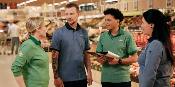 Vier Mitarbeiter in der Obst- und Gemüseabteilung beim Gespräch